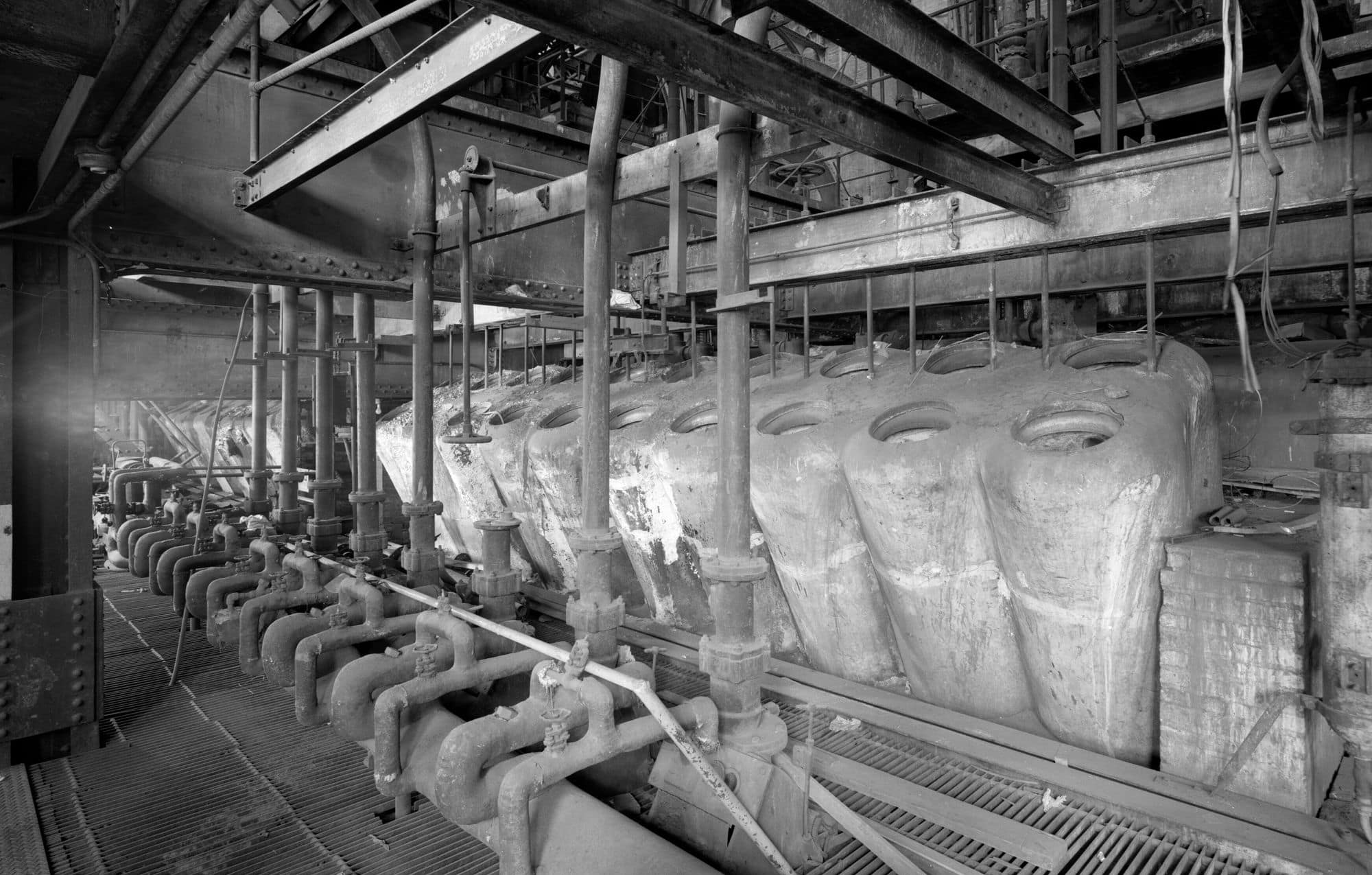 Black-and-white interior of a boiler house with oil burners and distribution headers