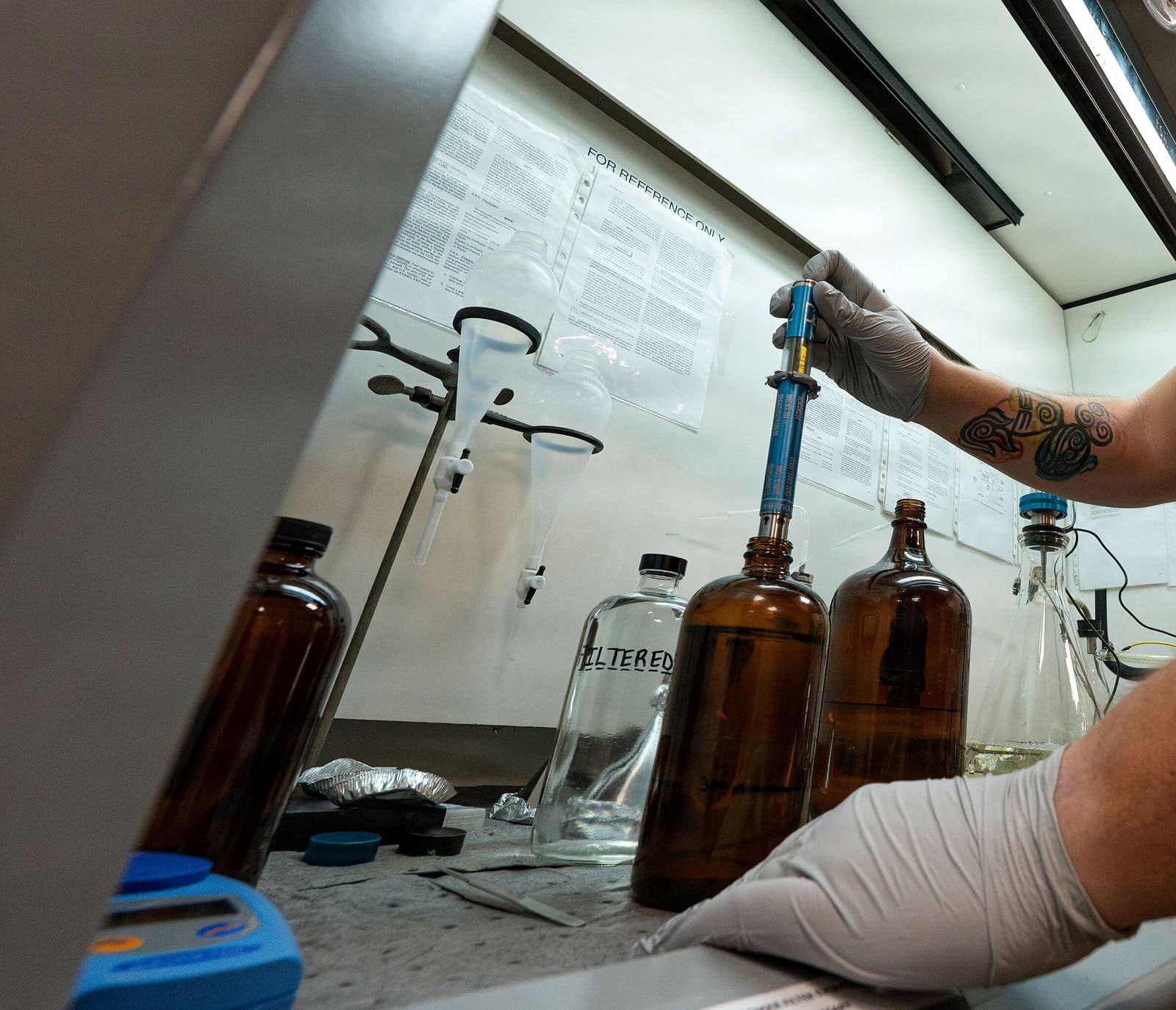Gloved hands handling fuel sample bottles in a laboratory fume hood